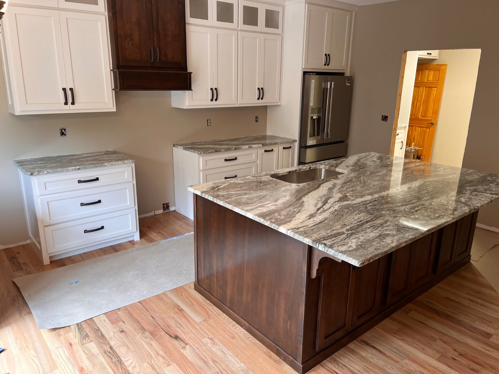 Kitchen countertop installed in Murphy, NC: Kitchen island with an undermount sink facing white perimeter cabinets and a fridge